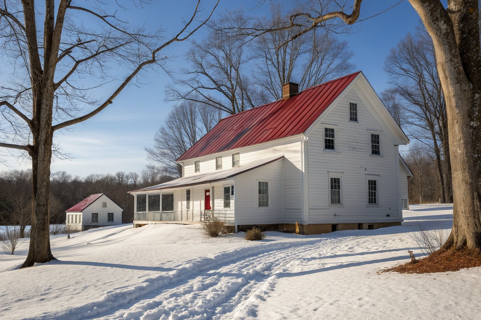 A white farmhouse with a red standing-seam metal roof in winter snow